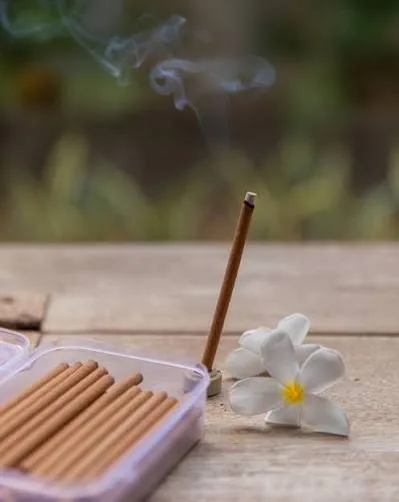 Natural dhoop stick burning outdoors beside a white frangipani flower
